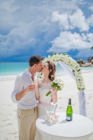 Hochzeit am Strand auf den Seychellen, romantisches Ja-Wort unter dem Blumenbogen.