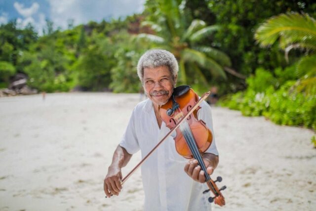 Mann spielt Geige am Strand auf den Seychellen bei einer perfekten Hochzeitsreise.