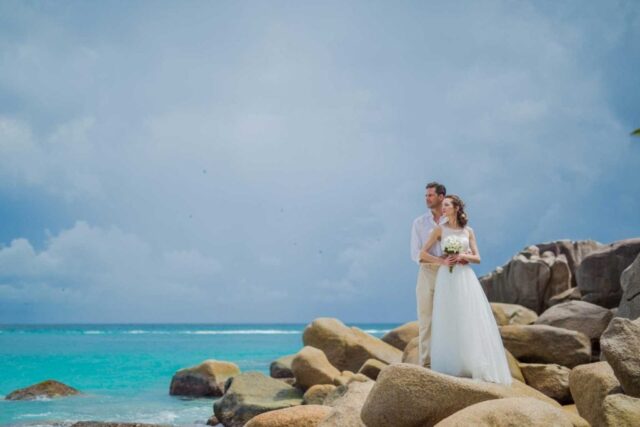 Traum Hochzeit Seychellen, Brautpaar am Strand mit Felsen, karibisches Flair, perfekte Hochzeitslocation, Inseltraum.